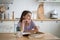 Thoughtful unconcentrated girl look to side doing homework sits at table with textbooks at kitchen