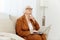 a thoughtful, wise, elderly woman writes an article on a laptop while sitting at home on the sofa in a comfortable