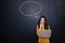 Thoughtful woman using laptop over chalkboard background with speech bubble