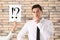 Thoughtful young businessman and female hand holding paper sheet with exclamation and interrogation marks against brick wall