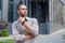 Thoughtful young businessman in glasses pondering outside modern office building, urban contemplation