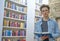 Thoughtful young man with a book in his hand standing in the library of a loft with a stone wall in the background