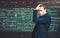 Thoughtful young man in elegant suit standing over green board full of writing. Anxious intelligent professor holding