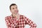 Thoughtful young man in hipster shirt holding hand on chin and standing against white background