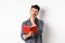 Thoughtful young man plan his schedule, looking aside pensive, holding opened planner or journal, standing on white