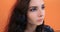 Thoughtful young pretty girl with long brown hair over orange wall background