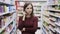 Thoughtful young pretty woman touches her face while she thinks about decision in supermarket