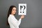 Thoughtful young woman holding sheet of paper with exclamation and interrogation marks on grey background