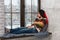 Thoughtful young woman lying down on the pillows on the windowsill and looking out the window while snowing