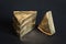 Thre triangular pieces of melted cream cheese wrapped in golden aluminium foil on black background. Portioned triangular cheeses