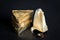 Thre triangular pieces of melted cream cheese wrapped in a golden aluminium foil and without packaging on a black background.