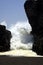 Threatening dangerous white sea wall pressing through rock gap on black lava sand beach at Pacific ocean