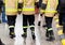 Three anonymous fireman in yellow reflective uniforms and black boots and trousers walking away from the camera