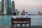 Three Arabic people sitting on a bench in Doha Cor niche and looking into the gulf