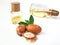 Three argan nuts with green leaves glass bottles on isolated white background. Chopped argan nut with a drop of oil