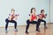 Three attractive sport girls doing squatting with dumbbells in fitness class.