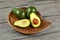 Three avocados, one of them cut to half, seed visible, in carved wooden bowl