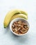 three bananas on top of a white bowl filled with granola