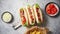 Three barbecue grilled hot dogs with sausage placed on wooden cutting board