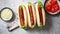 Three barbecue grilled hot dogs with sausage placed on wooden cutting board