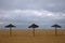 Three bast parasols on the sandy beach with bad weather