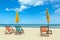 Three beach chairs with sun umbrella on beautiful beach with cloudy blue sky.