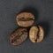 Three beans of high quality roasted coffee on a dark background close-up, macro photography, top view