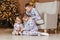 Three beautiful cheerful children in identical pajamas sit in chair and read a book for Christmas