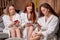 Three beautiful girlfriends relax using smartphones dressed in bathrobes after spa procedures