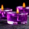 Three beautiful purple candles on a black background with water