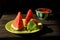 Three beautiful triangular slices of watermelon with juicy red pulp and black seeds on a green dish on a wooden table.