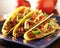 Three beef tacos with cheese, lettuce and tomatoes