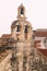 Three bells on an old stone bell tower against a background of tiled roofs