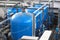 Three big blue water tanks inside wastewater treatment facility with many pipes and sensors, industrial interior