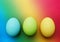 three biological organic blue turquoise apple green yellow easter eggs on a rainbow background
