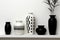 Three black and white vases sitting on a shelf. Generative AI image.