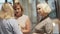 Three blonde haired women in elegant clothes having warm conversation standing in glassy hall.