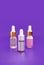 Three bottle of cosmetic oil, skin care serum on a purple background. Place for text