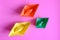 three bright colorful multicolor paper origami boats in orange, yellow and green colors on a pink background. flat lay, top view..