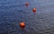 Three bright orange buoys floating on river water surface