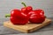 Three bright red bell peppers on old wooden cutting board.