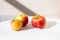Three bright ripe red apples iin the light of the sun with long shadows on a white background. One apple of an unusual shape of an