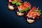 Three bruschetta sandwiches with jamon, tomatos, lettuce leaves and green sprouts on black.