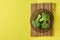 Three bunches of broccoli in dark round glass plate on bamboo rug lies on scratched yellow concrete desk on kitchen. Space for tex