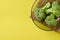 Three bunches of broccoli in dark round glass plate on bamboo rug lies on scratched yellow concrete desk on kitchen. Space for tex