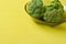 Three bunches of broccoli in dark round glass plate lies on scratched yellow concrete desk on kitchen