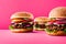 Three burgers on pink display.