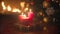 Three burning red Christmas candles on dinner table at living room next to fireplace and Christmas tree