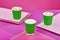 Three cappuccino coffee in paper green cups on a colorful pink background. Mockup. Cappuccino take away. Space for text.