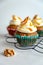 three carrot cake muffins with icing and carrot shaving on cooling rack white background